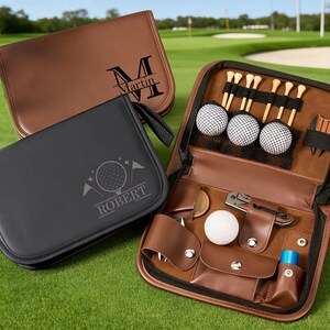 May include: A brown leather golf accessory kit with a black leather case. The kit includes golf balls, tees, and a multi-tool. The black case is personalized with the name "Robert". The brown case is personalized with the letter "M".
