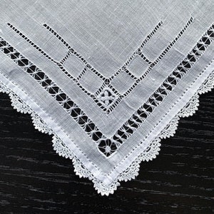 May include: White linen handkerchief with delicate lace edging and intricate embroidered details.