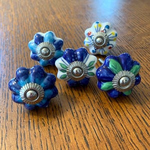 May include: Set of six blue and white ceramic flower-shaped cabinet knobs with silver accents. Each knob has a different floral design.