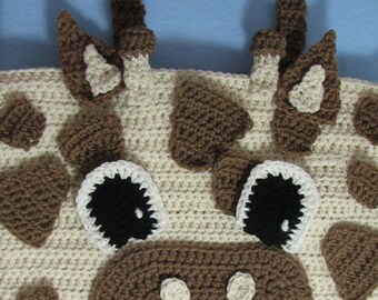 May include: A crocheted giraffe-shaped tote bag with brown spots and a brown nose. The bag has a brown handle and white eyes.