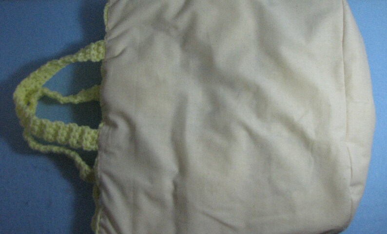 May include: A white canvas tote bag with a yellow crocheted handle. The bag is made of a soft, natural fabric and has a simple, classic design.