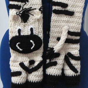May include: A crocheted zebra scarf with a black and white striped pattern. The scarf features a cute zebra face with black eyes and a white nose.