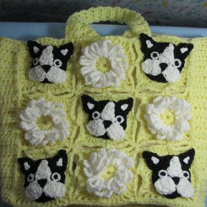 May include: Yellow crocheted tote bag with a square pattern featuring white crocheted flowers and black and white Boston Terrier dog faces.