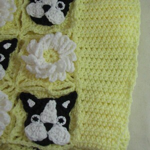 May include: A yellow crocheted baby blanket with a black and white crocheted dog design and white crocheted flowers.
