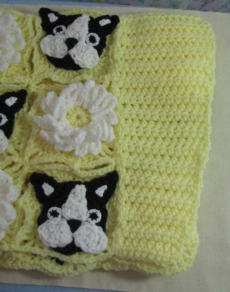 May include: A yellow crocheted baby blanket with a black and white crocheted dog design and white crocheted flowers.