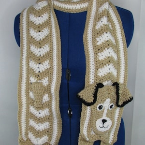 May include: A crocheted scarf with a brown and white chevron pattern. The scarf has a crocheted dog attached to it with black ears and eyes.