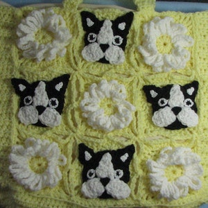 May include: A yellow crocheted tote bag with a repeating pattern of white crocheted flowers and black and white crocheted Boston Terrier dog faces.