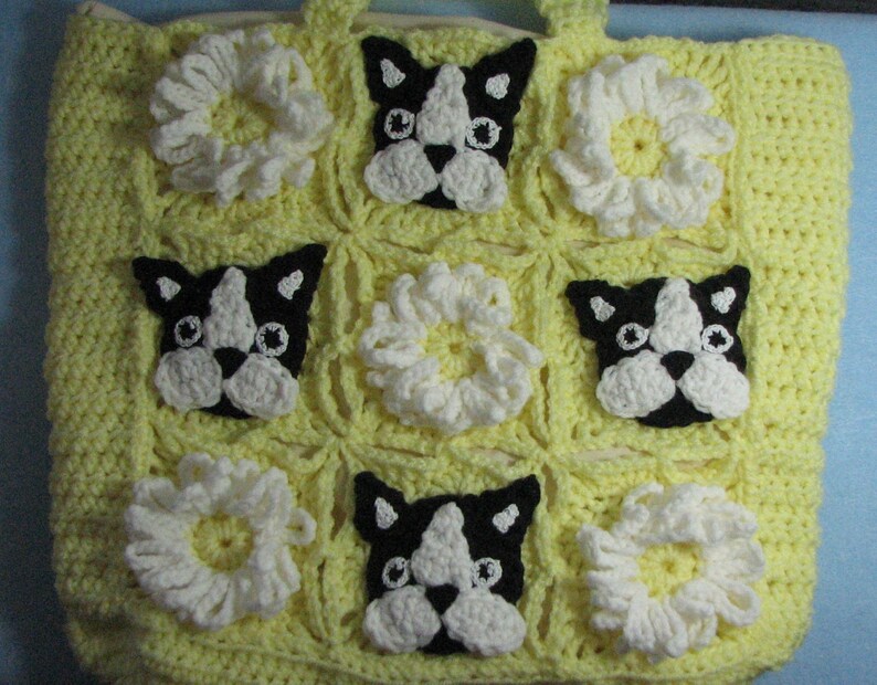 May include: A yellow crocheted tote bag with a repeating pattern of white crocheted flowers and black and white crocheted Boston Terrier dog faces.