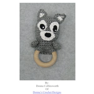 May include: Gray crocheted wolf teething ring with a wooden ring. The wolf has black eyes and a white nose. The ring is a light brown color.