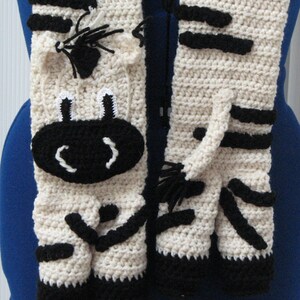 May include: A crocheted zebra scarf with black and white stripes. The scarf features a cute zebra face with black eyes and a white nose.