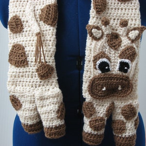 May include: A crocheted scarf with a brown and white giraffe pattern. The scarf has brown spots and a brown face with black eyes and a brown nose.