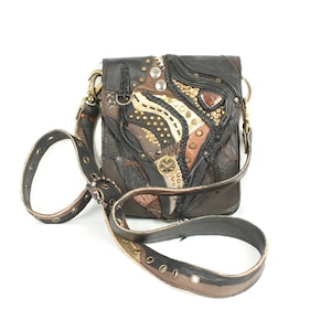 Puede incluir: Un bolso bandolera de cuero negro con un diseño de patchwork que presenta detalles en marrón, beige y dorado. El bolso tiene un cierre de solapa y una correa larga ajustable. El bolso está decorado con tachuelas metálicas y una variedad de adornos.
