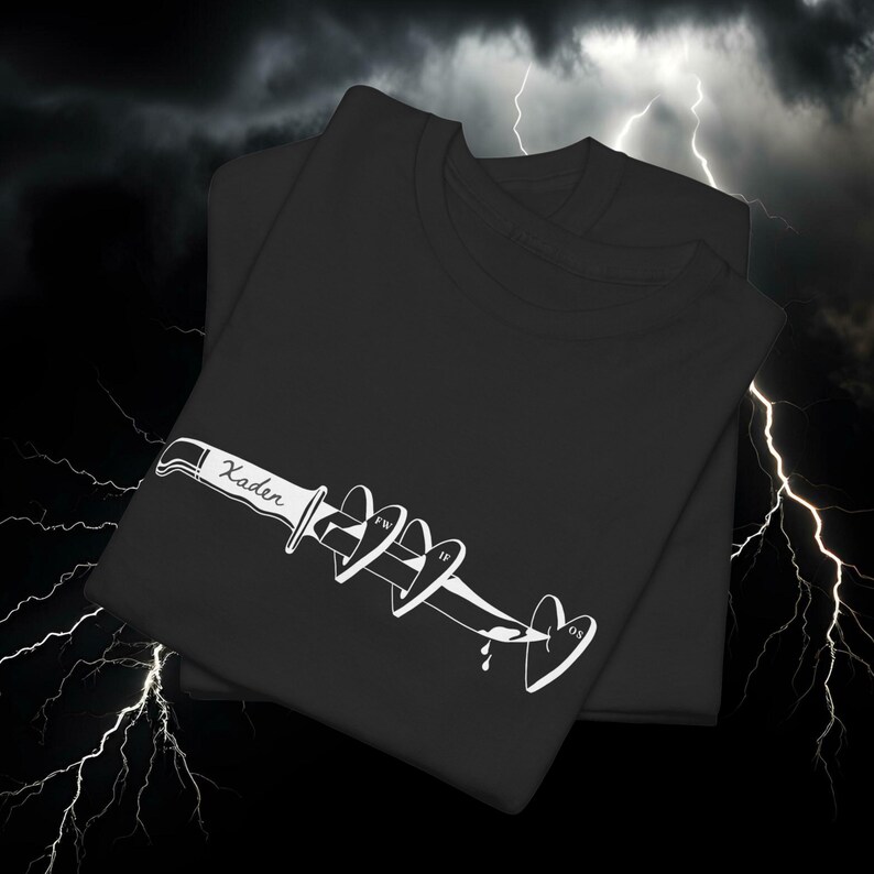 May include: Two black t-shirts with a white graphic design. The design features a knife piercing through a series of hearts, with the word "Kader" on the knife and the initials "FW", "IF", and "OS" on the hearts.