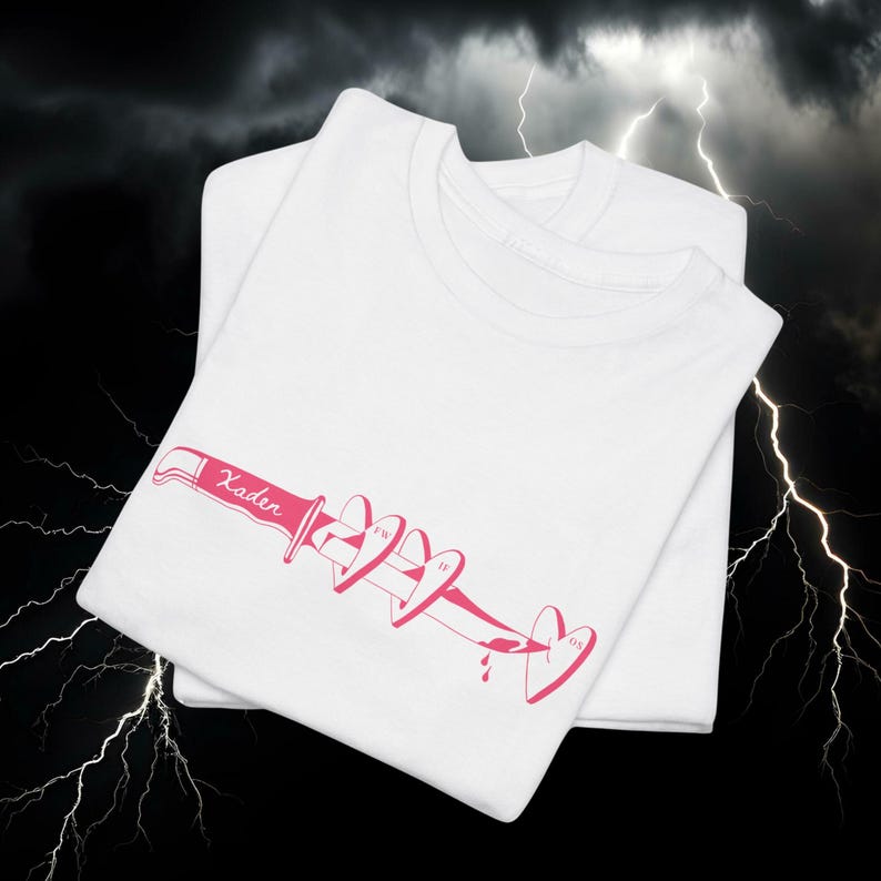 May include: Two white t-shirts are stacked, with the top shirt featuring a pink graphic of a knife piercing hearts. The word "Kader" is printed on the knife. The background is a dark sky with lightning.