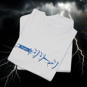 May include: Two light grey t-shirts are stacked, featuring a blue graphic of a knife piercing hearts. The word "Kaden" is above the knife. The graphic also includes the initials "FW", "IF", and "ON".