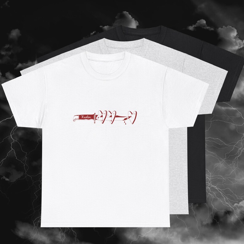 May include: White t-shirt featuring a red knife and heart graphic, with the word "Xaden" on the knife. The image shows three t-shirts in white, grey, and black, layered together.