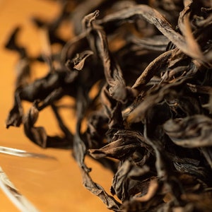 May include: Close-up of dried black tea leaves in a glass bowl. The leaves are curled and twisted, with a dark brown color.