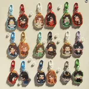 May include: A collection of anime-style character keychains. Each keychain features a colorful illustration of a character with a halo, attached to a metal clasp. The keychains have various colored borders and clasps, including red, blue, and green.