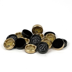 Pode incluir: Uma coleção de fichas com tema Bitcoin. Algumas fichas são douradas com um símbolo Bitcoin, enquanto outras são pretas com um símbolo "B" Bitcoin. As fichas têm formato circular e um verso de feltro.