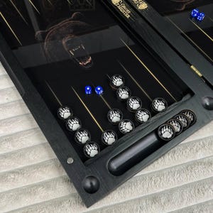 May include: A black backgammon board with a bear graphic and paw print game pieces. The board has gold accents and blue dice. The text "Gross Meister" is visible on the board.