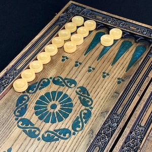 May include: A wooden backgammon board with a dark brown stain and intricate carvings. The board has a green felt playing surface with white playing pieces.