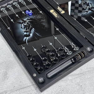 Puede incluir: Juego de backgammon negro con una ilustración de caballo. El tablero presenta un gráfico de caballo en blanco y negro, dados y fichas negras. El juego incluye un estuche negro con las palabras "Cross Meister".