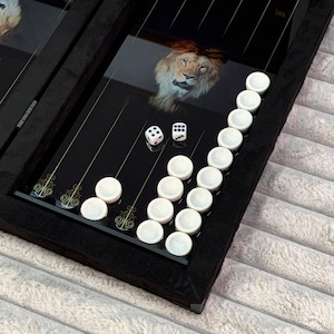 May include: A black backgammon game set with a lion image on the board. The game is open and shows white playing pieces and two dice.