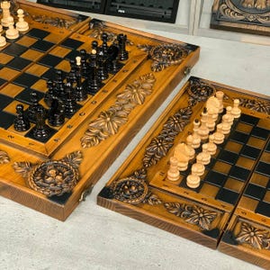 May include: Wooden chess and backgammon set with intricate floral carvings. The chess pieces are black and white, arranged on a checkered board. The backgammon board is also visible, with a similar carved design.