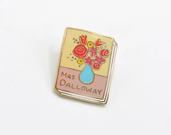 May include: Gold enamel pin featuring a book cover with a yellow background, pink and white stripes, and a blue vase with red, orange, and yellow flowers. The book title is "Mrs. Dalloway".