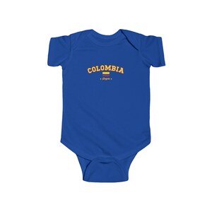 May include: A royal blue baby onesie with a yellow and orange graphic that says "COLOMBIA" with a small yellow and red flag underneath and the word "Shapes" in a smaller font.