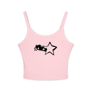 May include: A light pink camisole top with thin straps. The top features a black graphic of an eye and a star. The design is centered on the front of the top. The top is made of a soft, ribbed material.