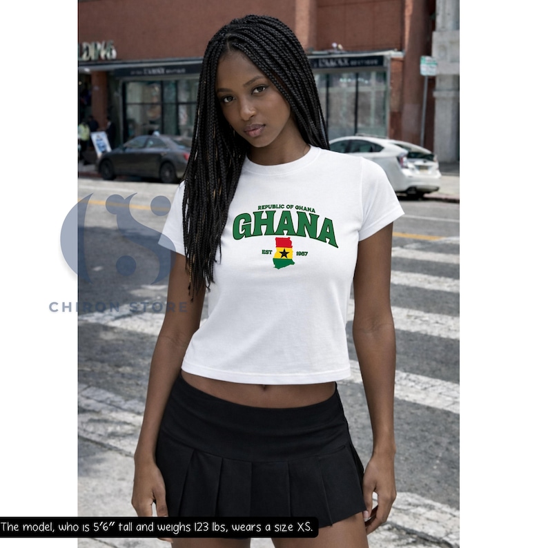 May include: A white short-sleeved t-shirt featuring the green text Republic of Ghana and Ghana arched above a graphic of the Ghana flag with the text EST 1957 below it. The shirt is paired with a black pleated mini skirt.