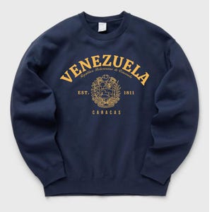 May include: Navy blue sweatshirt with a gold design featuring the word "VENEZUELA" in an arch, the text "Republica Bolivariana de Venezuela", a coat of arms, and the text "EST. 1811 CARACAS".