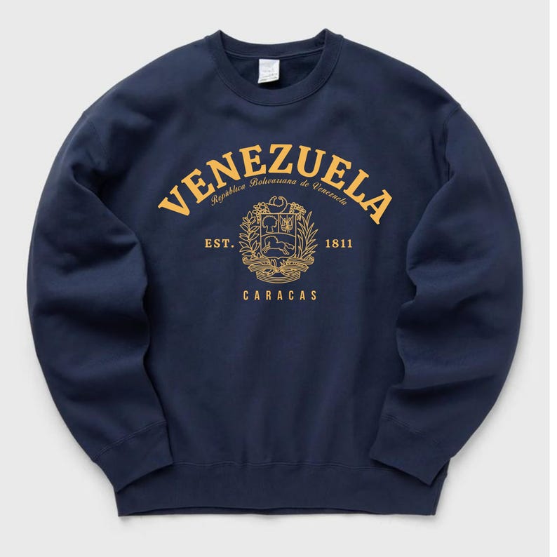 May include: Navy blue sweatshirt with a gold design featuring the word "VENEZUELA" in an arch, the text "Republica Bolivariana de Venezuela", a coat of arms, and the text "EST. 1811 CARACAS".