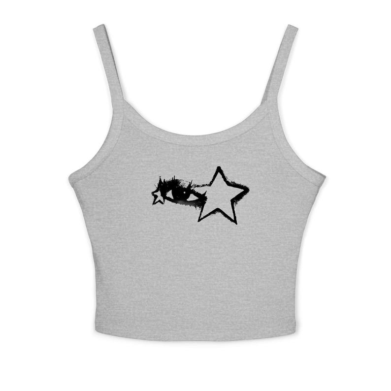 May include: A light gray tank top with thin straps. The front features a black graphic of an eye and two stars. The design has a hand-drawn, grunge aesthetic. The top is made of a soft, likely cotton material.