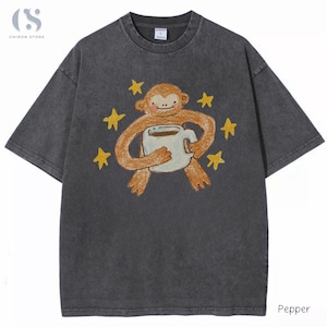 May include: A charcoal grey short-sleeve t-shirt with a crew neckline. The centre features a graphic of a light brown monkey holding a white mug filled with dark liquid, surrounded by six yellow stars. The design has a textured, crayon-like appearance.