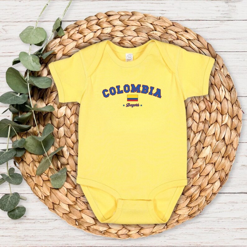 May include: Yellow baby onesie with a blue and yellow Colombian flag and the text "COLOMBIA *Bogota*" in blue.