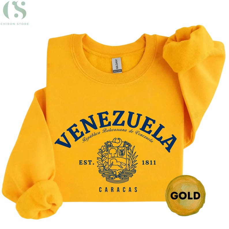 May include: A gold-colored sweatshirt with the word "VENEZUELA" in navy blue arched across the front. Below the word is a crest and the words "EST. 1811 CARACAS". The sweatshirt has a round neck and long sleeves.