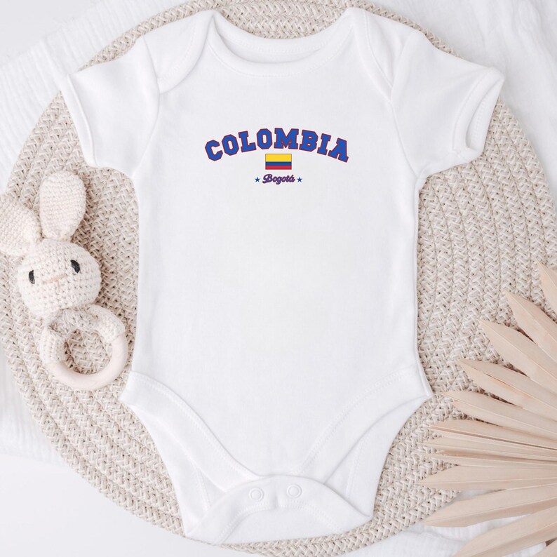 May include: White baby onesie with a blue and yellow Colombian flag and the text "COLOMBIA *Bogota*" in blue.