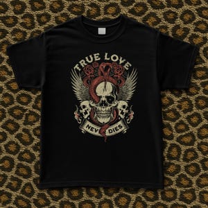 Pode incluir: T-shirt preta com um design de caveira, cobra, rosas e asas. O texto "TRUE LOVE NEVER DIES" &eacute; exibido acima e abaixo da caveira. O gr&aacute;fico &eacute; em tons de vermelho, branco e bege.