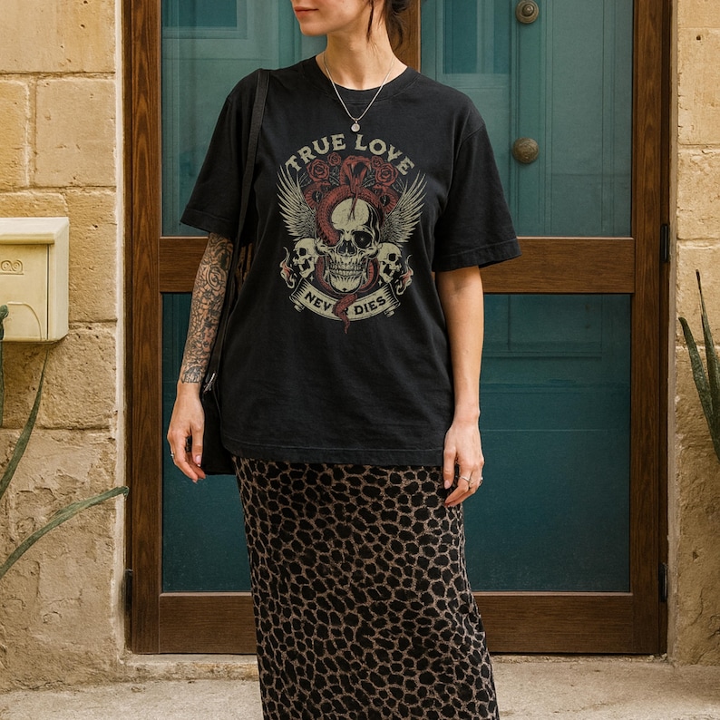 Pode incluir: Camiseta preta com um design gr&aacute;fico com uma caveira, asas e as palavras "TRUE LOVE NEVER DIES". A camisa &eacute; combinada com uma saia longa com estampa de leopardo. Uma bolsa preta tamb&eacute;m &eacute; vis&iacute;vel.