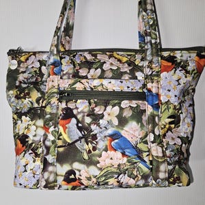 Bolso de mano de tela acolchada con hermosos pájaros sobre un fondo de flores y vegetación