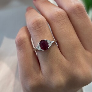 Op de afbeelding: Een zilveren ring met een grote ovale robijn en twee kleinere diamanten.