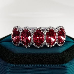 Op de afbeelding: Een ring met vijf ovale rode edelstenen gezet in een zilveren band. Elke edelsteen is omgeven door een halo van kleinere witte edelstenen.