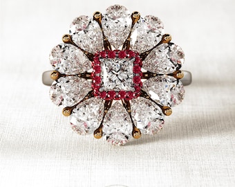 May include: A gold ring with a large, square-shaped diamond surrounded by smaller diamonds and red rubies. The ring is set in a flower-shaped design.