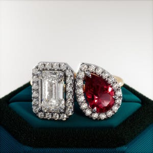Può includere: Due anelli con gemme. Uno presenta un diamante taglio smeraldo circondato da un alone di diamanti. L'altro ha una gemma rossa a forma di pera, anch'essa con un alone di diamanti. Entrambi gli anelli sono montati su fasce d'oro.