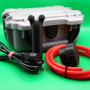 Puede incluir: Una maleta gris de caparazón duro con cierres negros, un cable de alimentación negro, un objeto cilíndrico negro, una manguera roja y una tapa negra. El objeto cilíndrico tiene el texto "MillionfanShop" impreso.