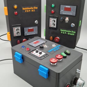 Może przedstawiać: Trzy czarne skrzynki kontrolne z różnymi przyciskami, przełącznikami i wyświetlaczami cyfrowymi. Pudełka mają pomarańczowe, zielone i niebieskie akcenty. Tekst na pudełkach zawiera "Reduktionsfan Shop" i "Speed Controller."