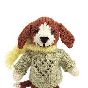 May include: A knitted brown and white dog wearing a green jumper with a heart design and a yellow scarf.