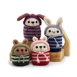 May include: Four knitted stuffed animals wearing striped hooded sweaters. The animals are a dog, a bunny, a bear, and a cat. The animals are all sitting on a wooden platform.
